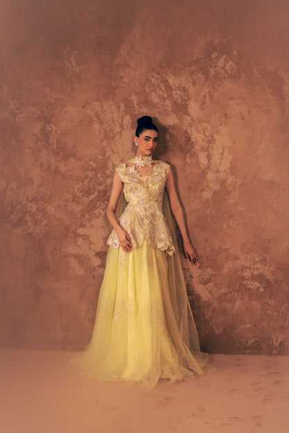 Model leaning on wall in Blooming Dawn designer Pakistani formal dress with flared pants, net dupatta drape and embroidered peplum