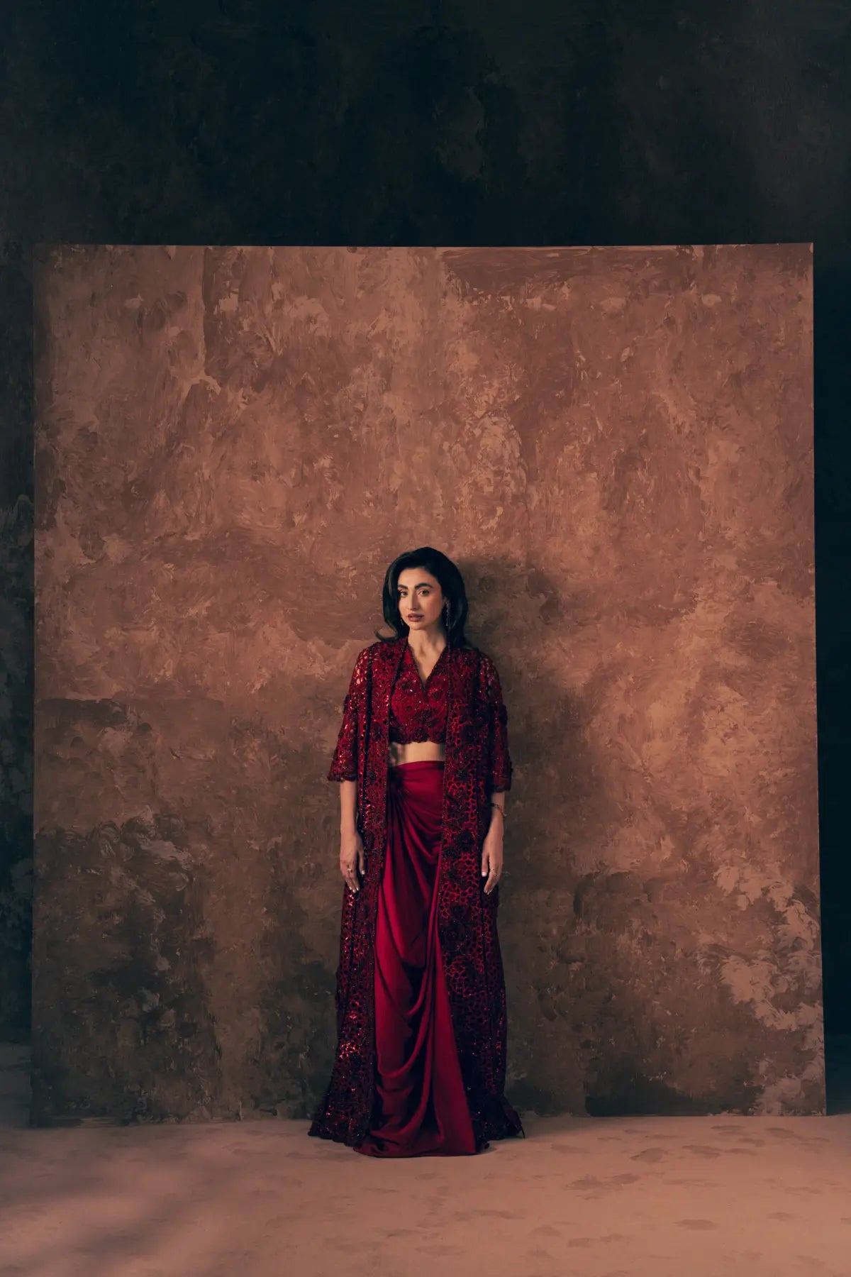 Model wearing Crimson 3 piece Pakistani formal dress with long cutwork jacket, embroidered blouse and draped satin silk skirt