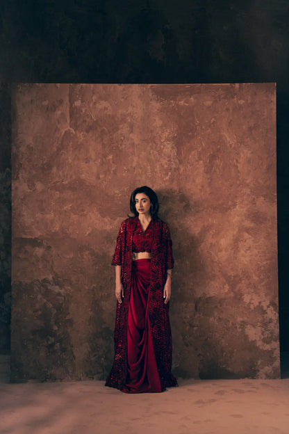 Model wearing Crimson 3 piece Pakistani formal dress with long cutwork jacket, embroidered blouse and draped satin silk skirt